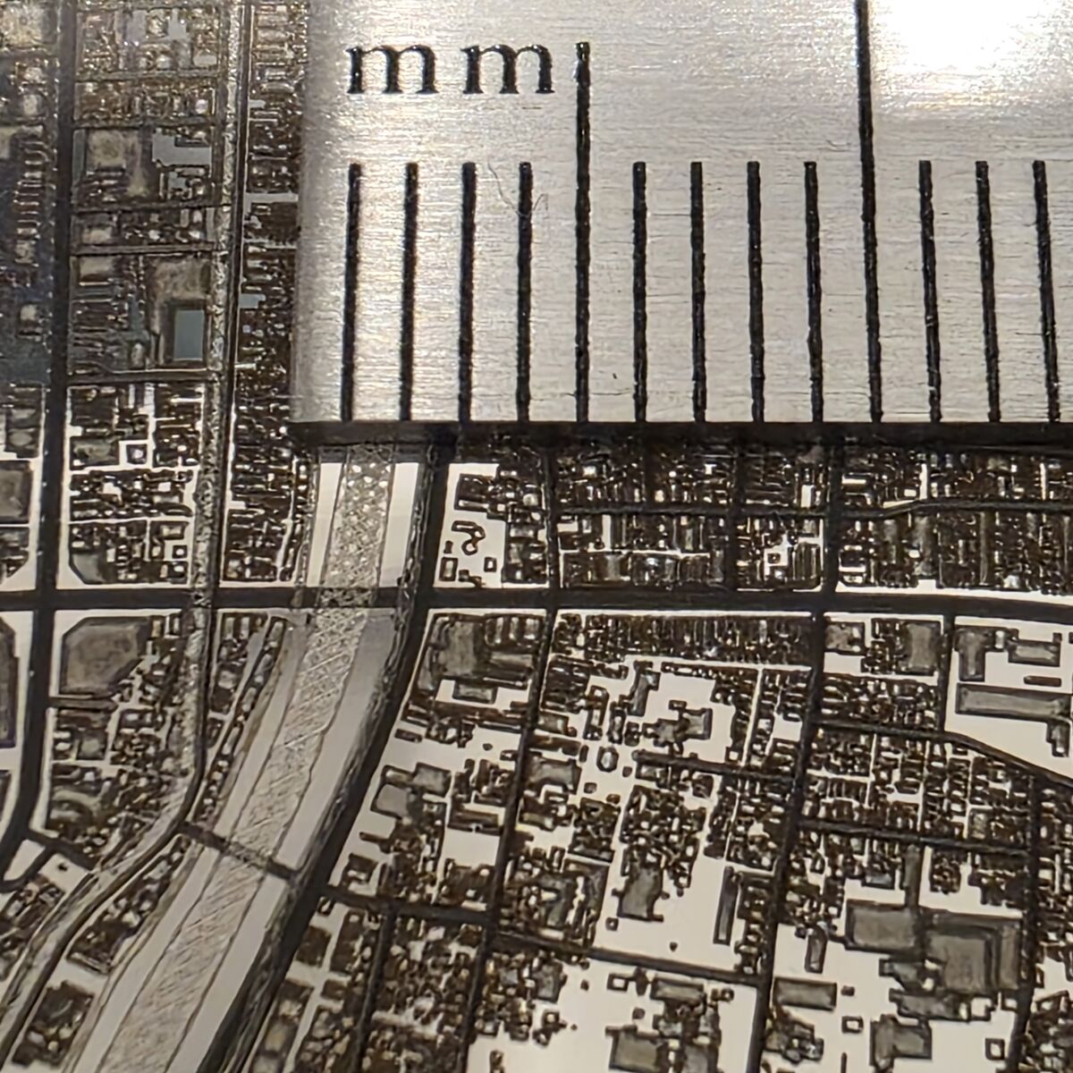 A macro photograph of a dense old town centre engraved on a coin beside a millimetre ruler, with hundreds of tiny buildings, a canal and narrow lanes