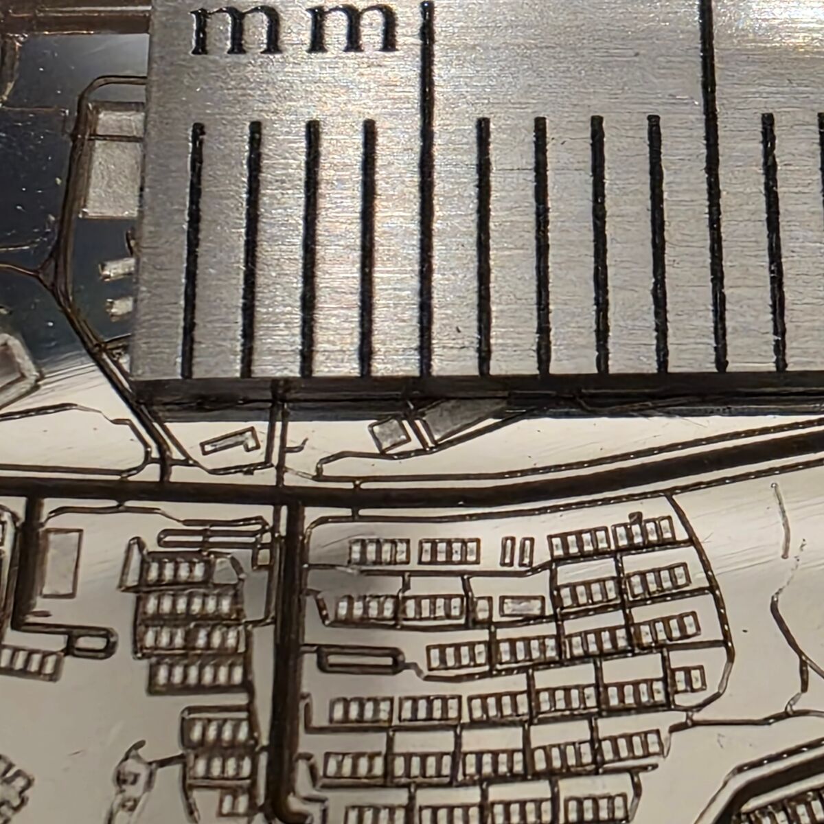 A macro photograph of terraced houses engraved on the coin, next to millimetre ticks on a ruler; each row of houses is about one tick long