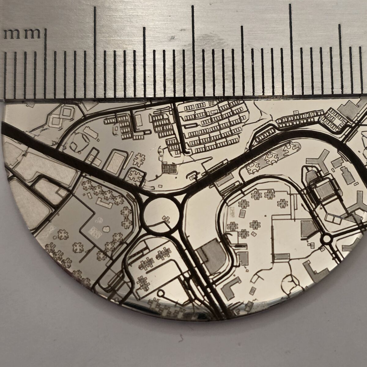 The same coin beneath a steel millimetre ruler, showing rows of houses and a roundabout each only a few millimetres across